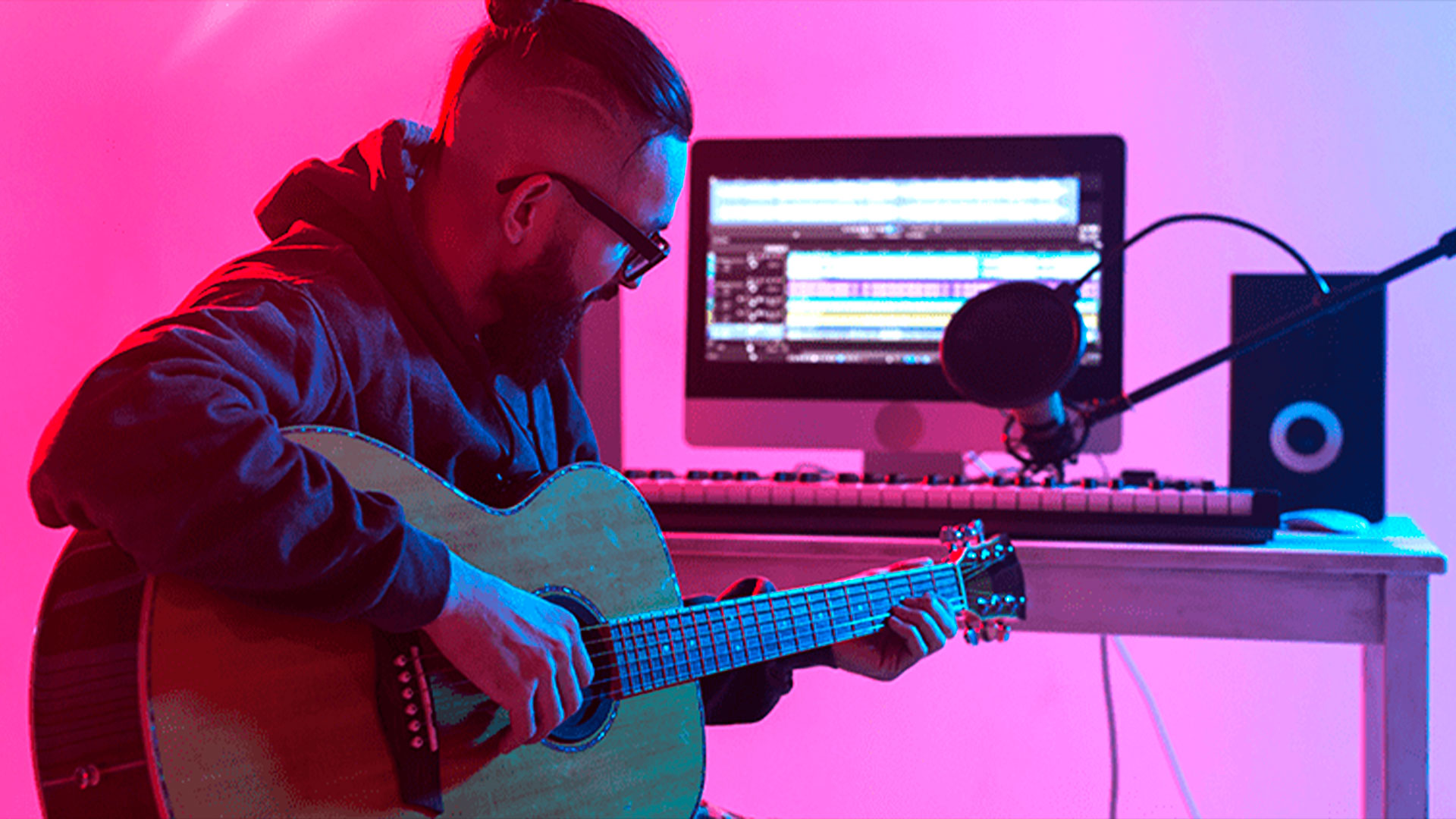 Guitarrista junto a computadora, microfono y monitor de estudio